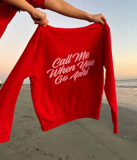 Red sweatshirt with text held by a person on a beach at sunset